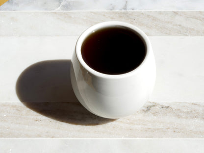 White mug filled with dark tea on a marble surface