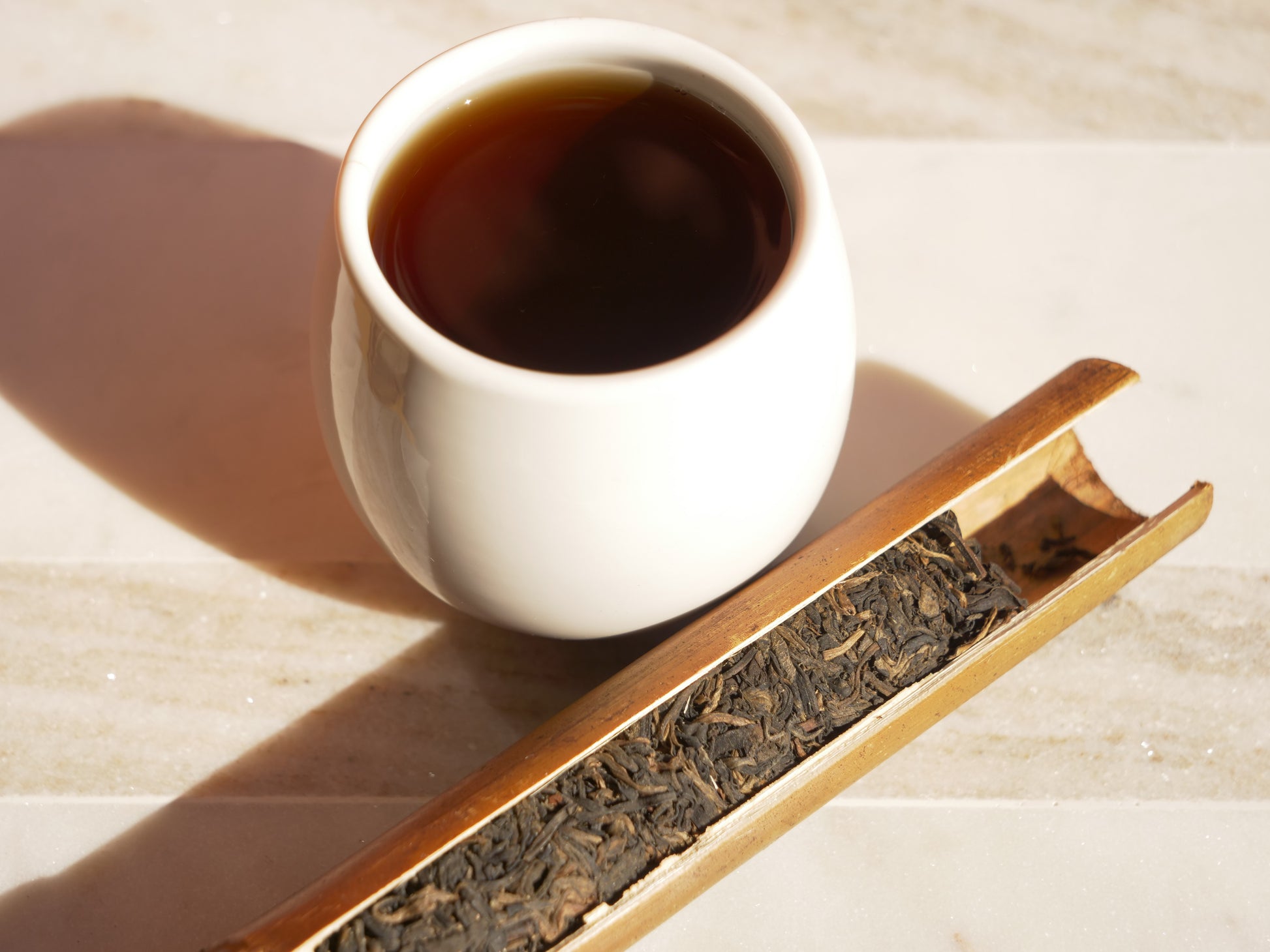 White cup of dark tea with a bamboo tube full of tea leaves.