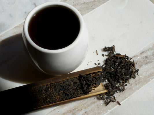 White cup of dark tea with tea leaves on a marble surface