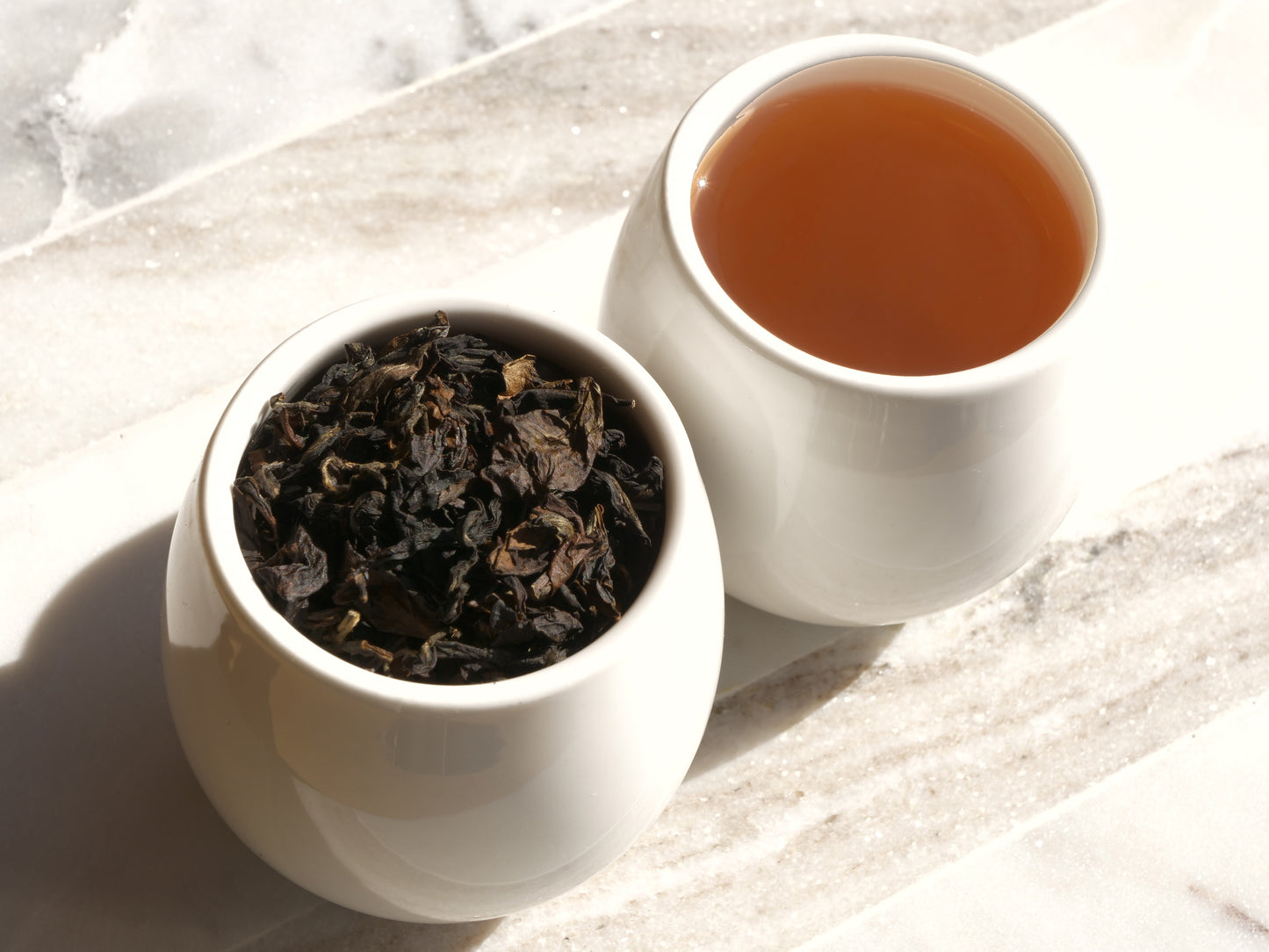 White container with tea leaves and a cup of brewed tea on a marble surface
