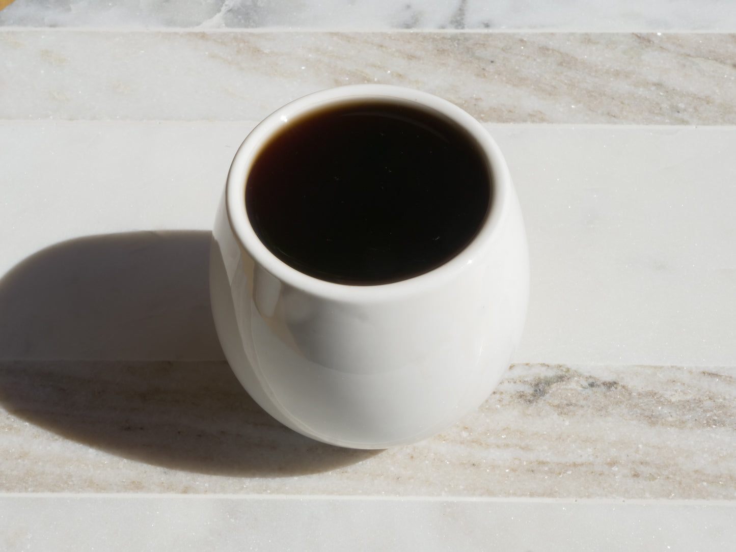 White ceramic mug filled with dark tea on a marble surface