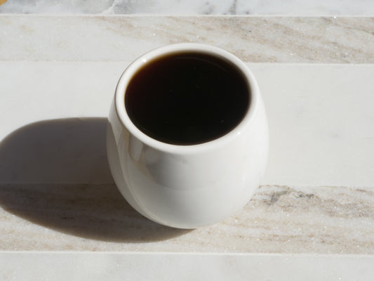 White ceramic mug filled with dark tea on a marble surface