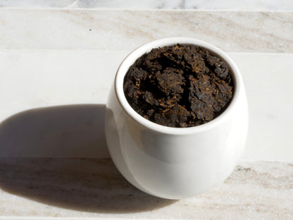 White container filled with tea leaves on a light marble surface