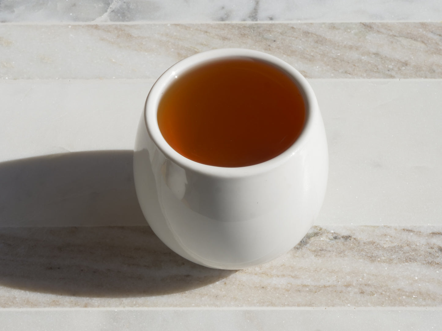 White ceramic cup filled with brewed tea on a marble surface