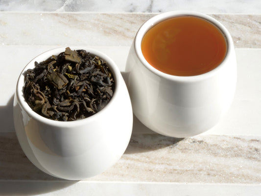 White bowl with tea leaves and a cup of brewed tea on a marble surface