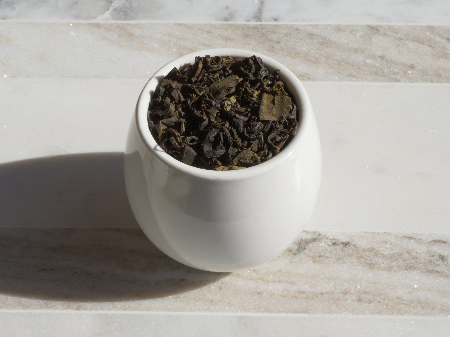 White ceramic container filled with tea leaves on a marble surface