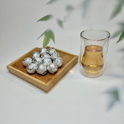 White tea pearls wrapped in foil next to a glass of brewed tea.
